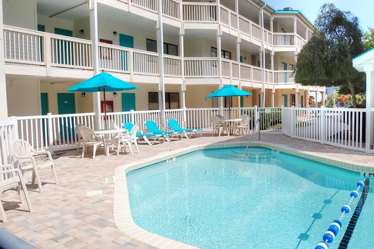 An inviting outdoor pool area is shown, complete with lounge chairs, umbrellas, and visible balconies above. The image captures a relaxing, resort-style mood, ideal for sunbathing, swimming, and socializing just steps from the condo.