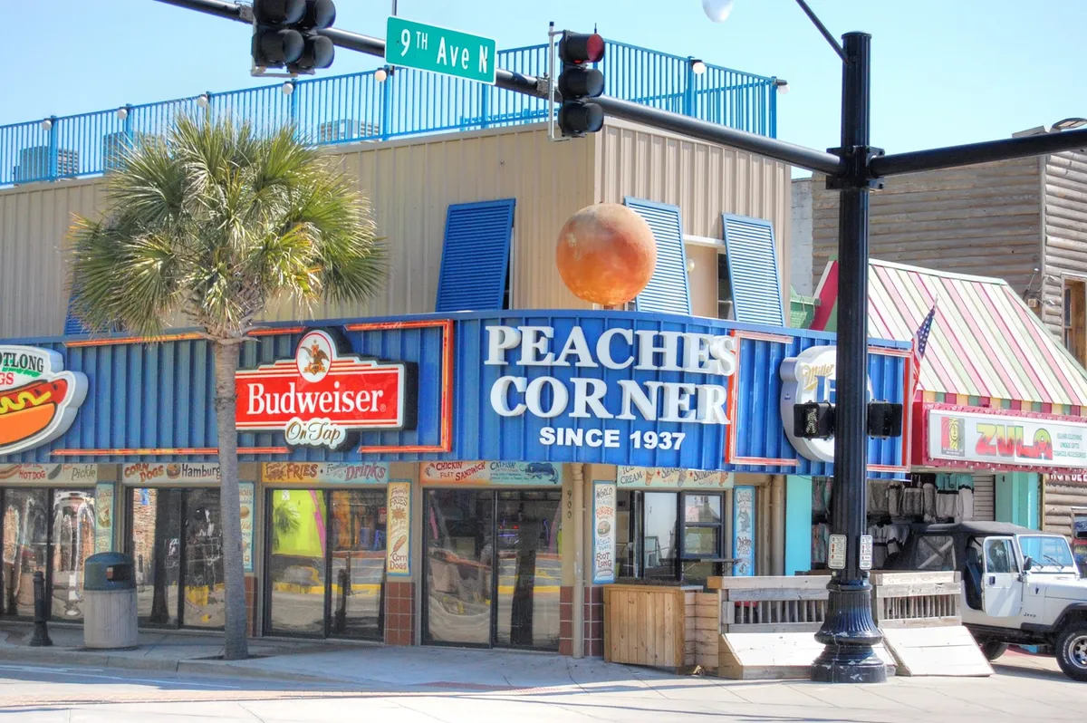 This vibrant exterior image features the colorful Peaches Corner and Budweiser signs, the building’s signature orange ball, and palm trees. The festive energy of the area hints at the lively dining and nightlife options nearby.