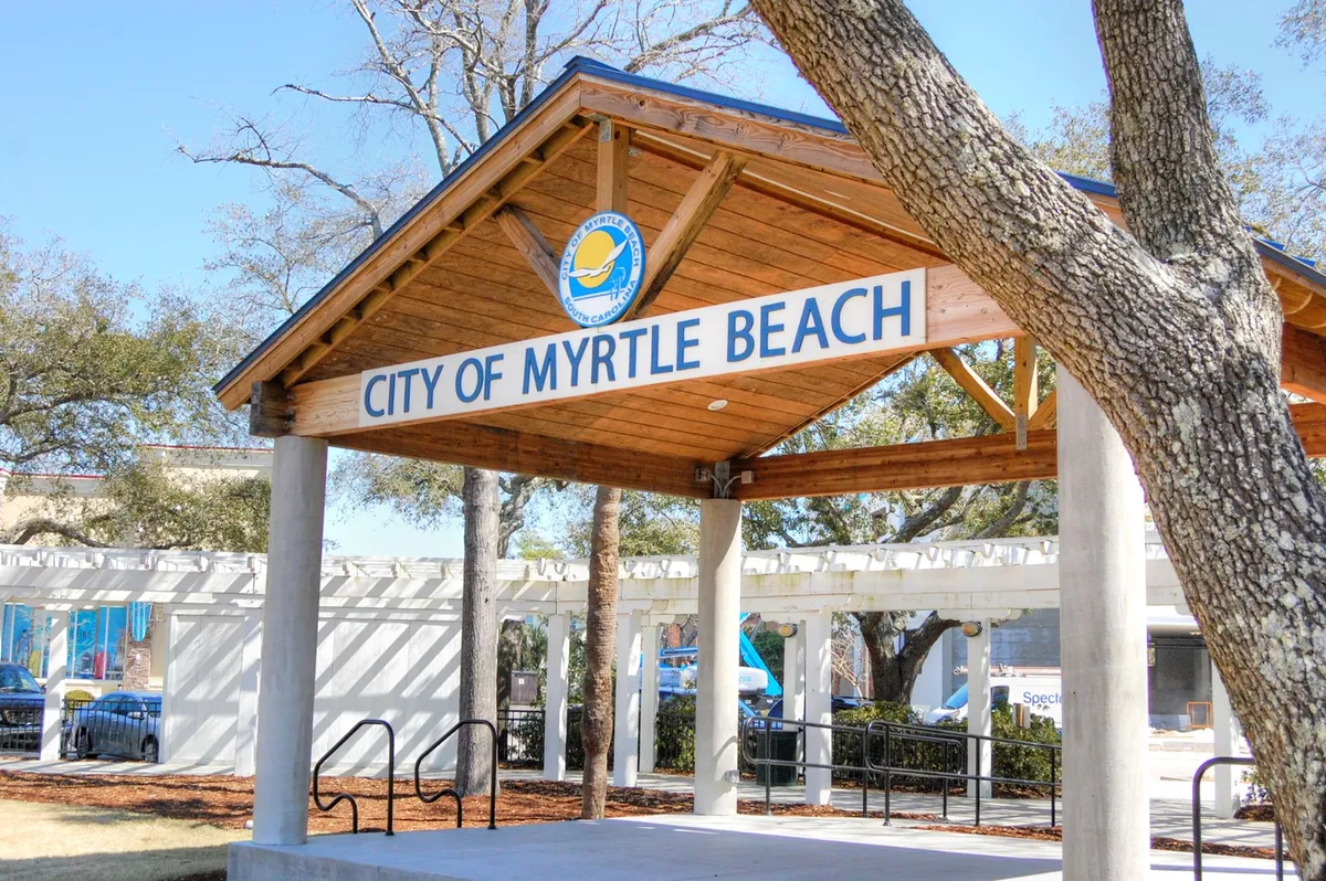 An inviting exterior shot of a wooden structure bearing the 'CITY OF MYRTLE BEACH' sign, surrounded by trees. The space appears open and welcoming, suggesting community connections and a sense of place. This image highlights the local character and the broader environment guests can explore.