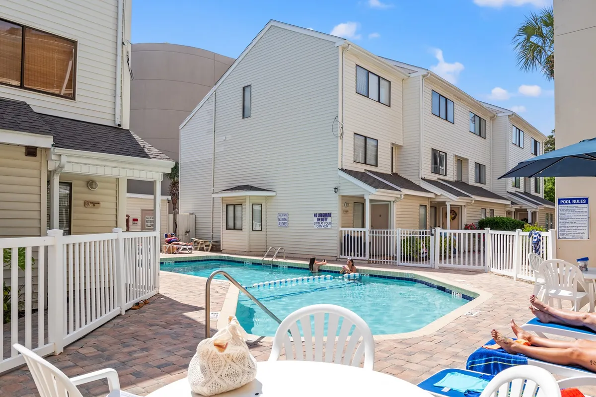 This exterior image captures the inviting resort swimming pool area surrounded by townhouse exteriors and comfortable poolside seating. The space is ideal for casual group gatherings, swimming, and sunbathing, offering a glimpse of the social atmosphere guests can expect at Ocean Dunes Villas.