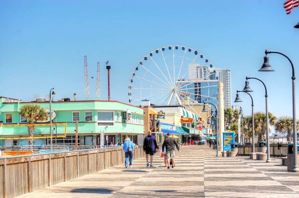 This lively exterior image captures a bustling boardwalk with a ferris wheel, colorful buildings, palm trees, and visitors strolling along. It radiates excitement and offers a snapshot of Myrtle Beach’s iconic family-friendly attractions, shopping, and entertainment options.